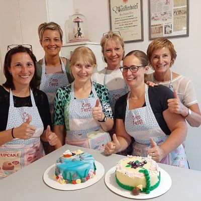 Freundinnen backen gemeinsam Torten mit einer Unterwasserwelt und einem Garten mit Blumen